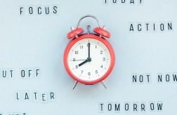 Picture of a red clock on a blue background with various time management related words surrounding it like focus, today, action, tomorrow
